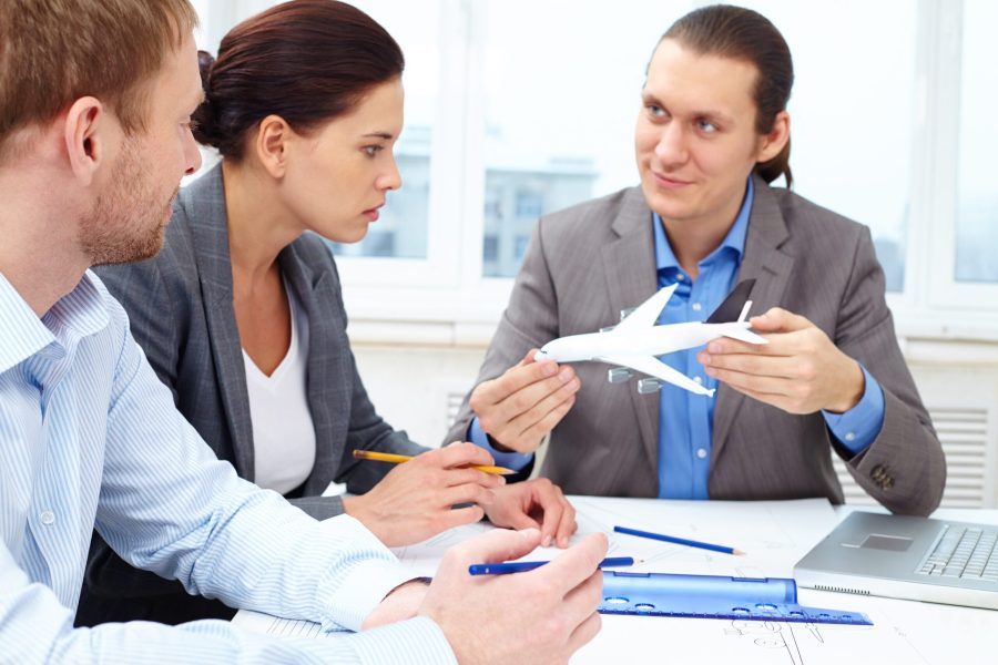 Three engineers discussing a small model of a plane while making its sketch